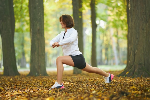 Happy female in sport outfit stretching body at park