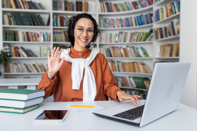 Happy female tutor in headset sits in front of laptop in classroom conducts online classes smiles