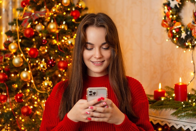 Happy female using mobile phone in living room decorated for Christmas