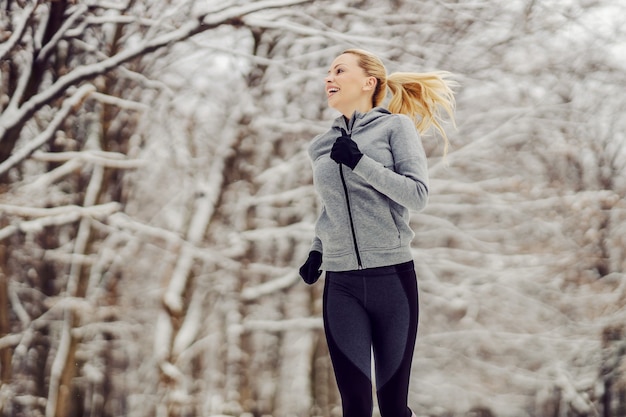 Happy fit sportswoman jogging in nature at snowy winter day. Healthy life, winter sport