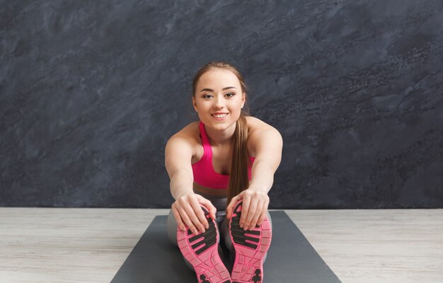 Happy fitness woman warmup stretching, training at grey background indoors. Young slim girl making yoga exercise, closeup of foot, copy space