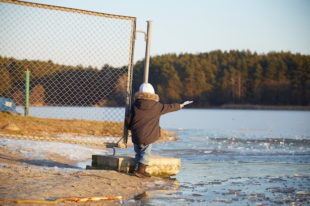 Happy four year old child throwing piece of ice into the river