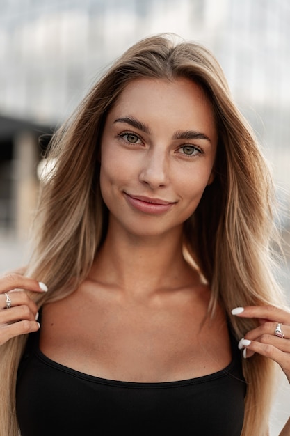 Happy fresh portrait of beautiful fashion blonde girl with green eyes in black tank top looks at the camera on the street, close-up