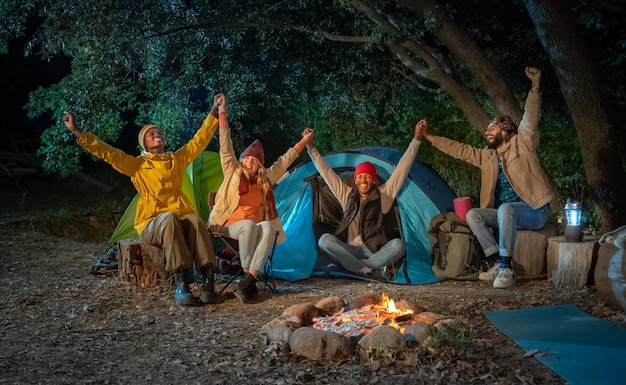 Happy friends celebrate and have fun laughing together with arms raised bonfire on camping