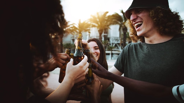 Happy friends cheering beer bottles on summer sunset background