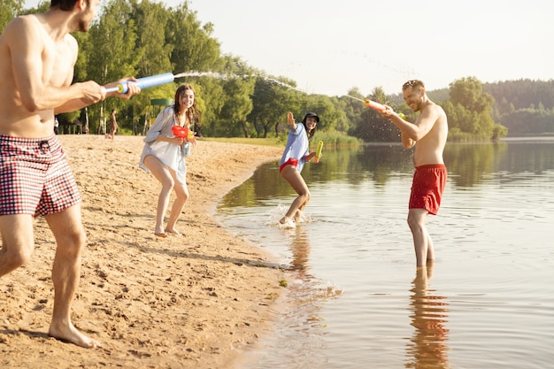 Happy friends doing battle with water guns - Youth, summer lifestyle and holiday concept