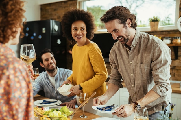 Happy friends enjoying while setting dining table for lunch. Focus is on young man.