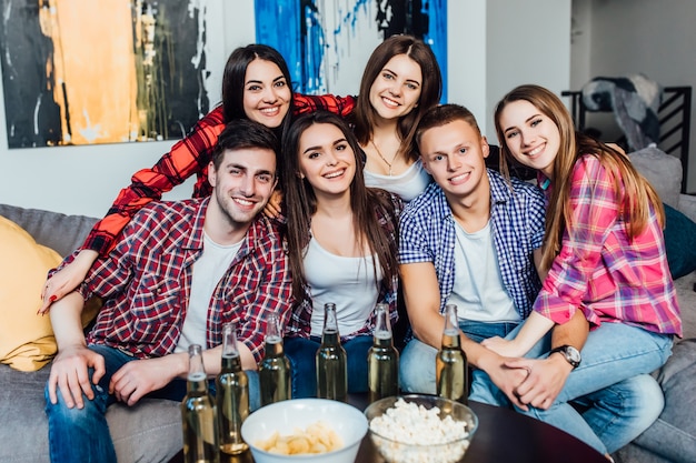 Happy friends or football fans watching soccer on tv and celebrating victory at home. Eating popcorn and drink beer.