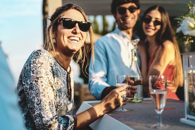 Happy friends gathering at terrace party having fun and drinking sparkling white wine life style concept of young people hangout on weekend talking and consuming alcoholic drinks