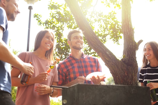 Happy friends grilling meat and enjoying barbecue party outdoors.