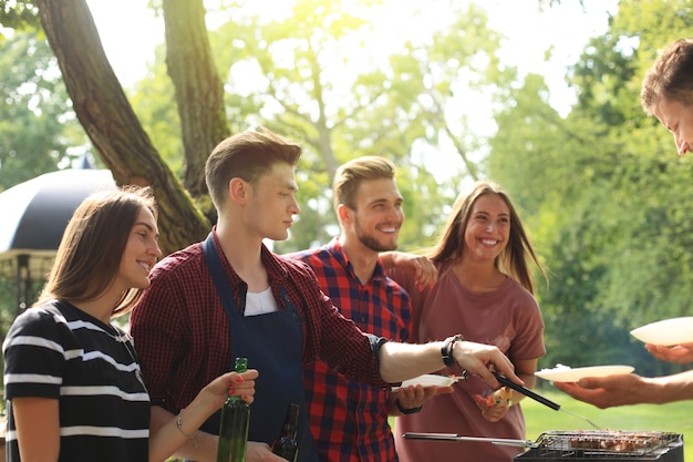 Happy friends grilling meat and enjoying barbecue party outdoors.