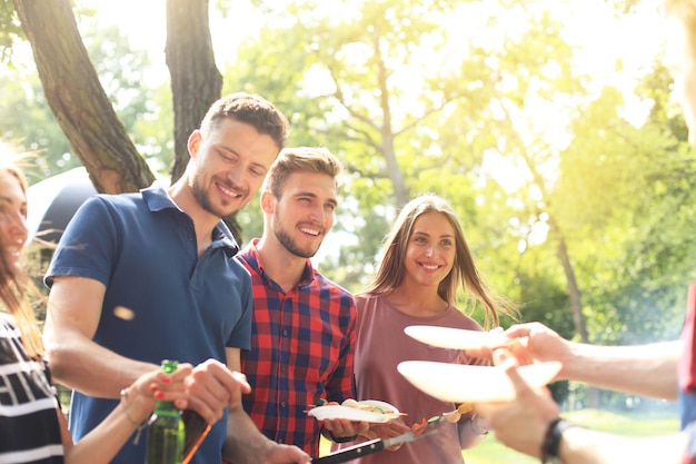 Happy friends grilling meat and enjoying barbecue party outdoors.