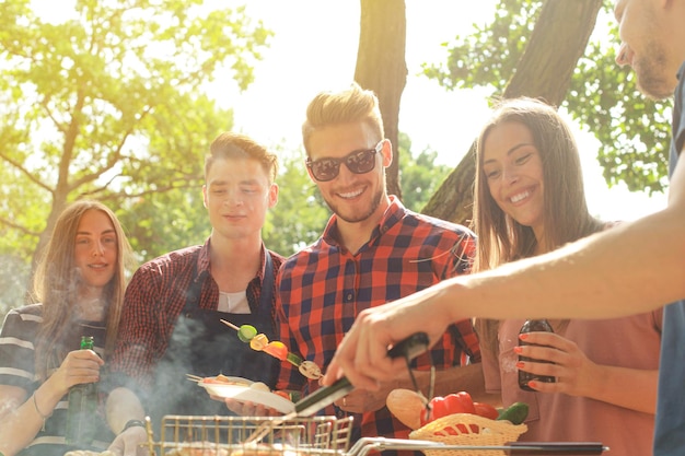 Happy friends grilling meat and enjoying barbecue party outdoors