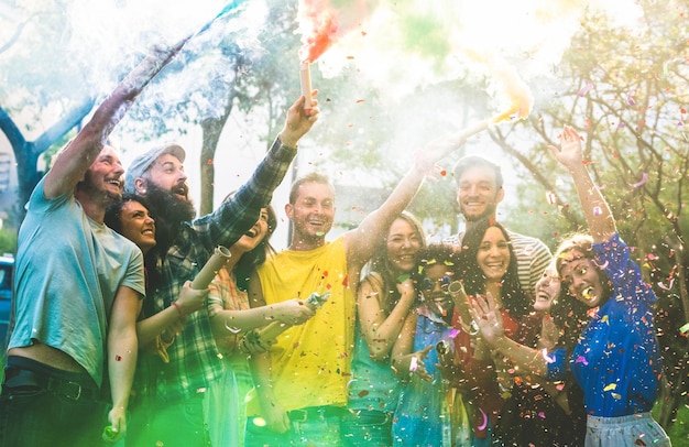 Happy friends having fun at garden party with multicolored smoke bombs outdoor