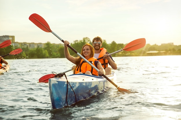 Happy friends kayaking on river with sunset on the background