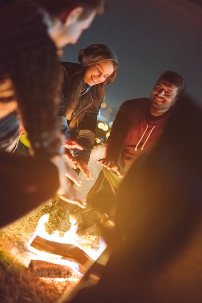 The happy friends warming hands near a bonfire. evening night time