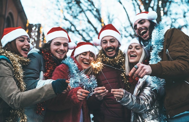 Happy friends wearing santa claus hat celebrating Christmas day holding sparklers