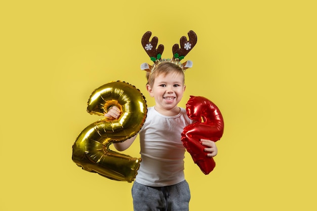 Happy funny child boy in red Christmas reindeer costume with balloon numbers