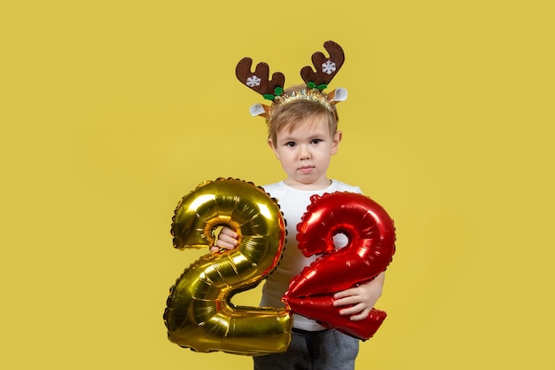 Happy funny child boy in red Christmas reindeer costume with balloon numbers