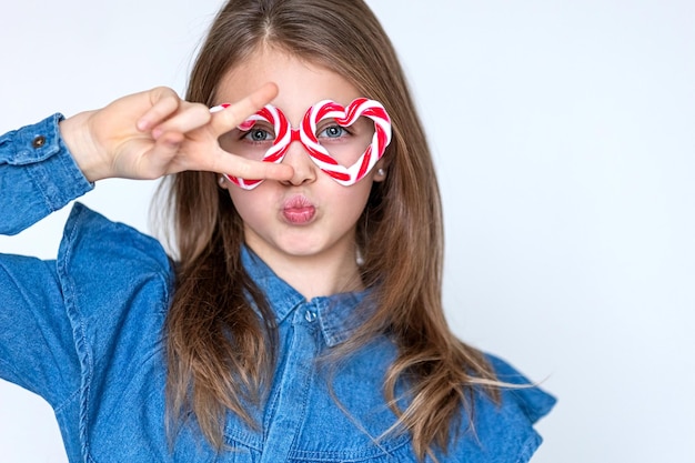 Happy funny little girl in caramel glasses looks at the camera with hearts and smiles Valentines day background Copy space for text