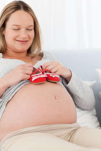 Happy future mom putting baby shoes on her belly