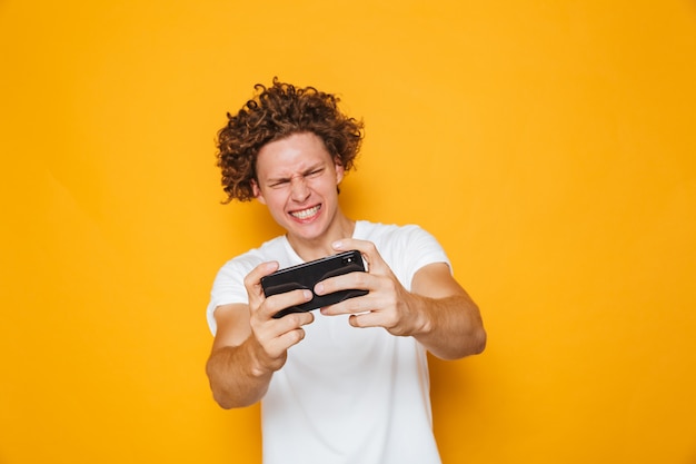 Happy gamer man in casual t-shirt playing online video games on smartphone