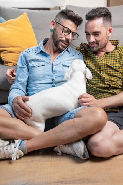 Happy gay couple sitting on floor and playing with dog at home