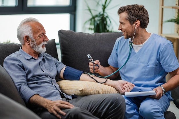 Happy general practitioner measuring blood pressure of mature man while being in a home visit