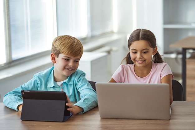 The happy girl and a boy with a tablet and a laptop sitting at the table