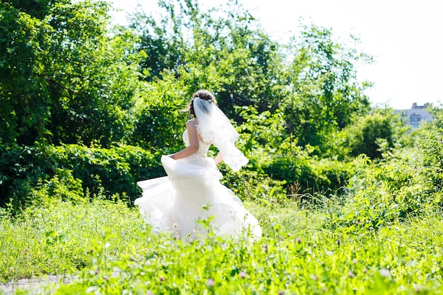 Happy girl bride in a long white wedding dress and in a veil swirl in a green park on nature.