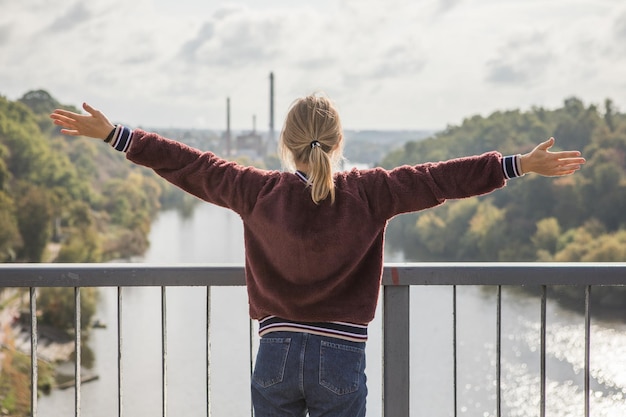 Happy girl on the bridge and feeling free and looking at the blue river