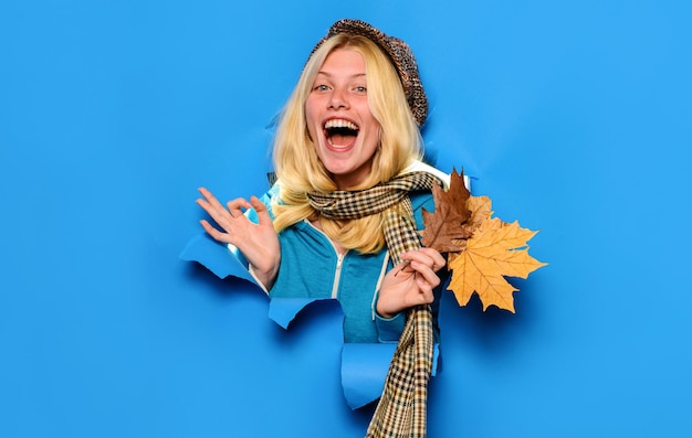 Happy girl in cap and scarf with maple leaves showing ok sign autumn sales discount black friday