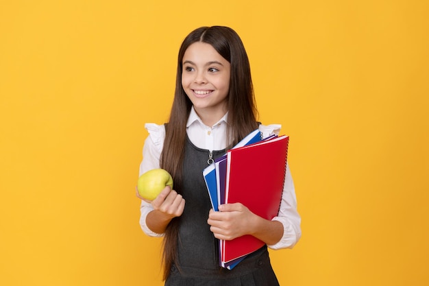 Happy girl child back to school holding apple and books yellow background knowledge day