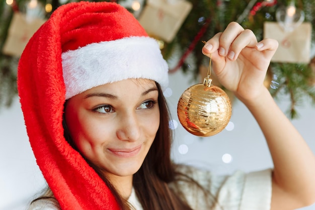 happy girl in a Christmas hat with a Christmas tree toy in her hand closeup