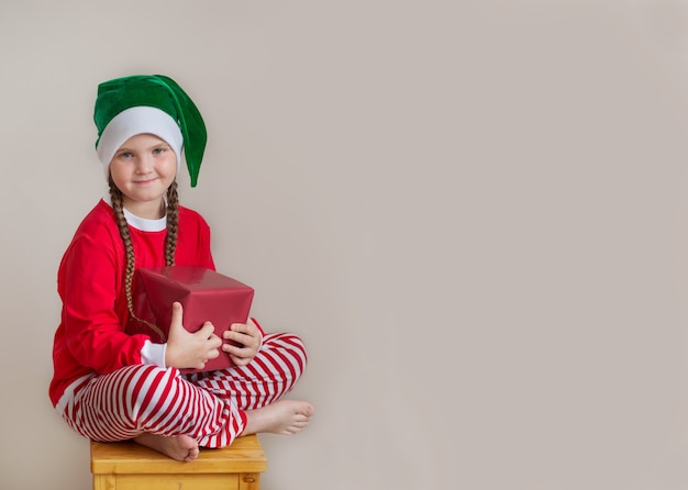 Happy girl in christmas pijamas with christmas gift on gray