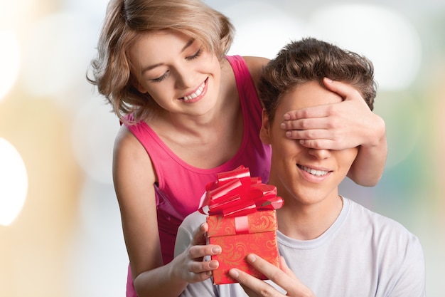 Happy girl covering her boyfriend's eyes with hands and gives gift