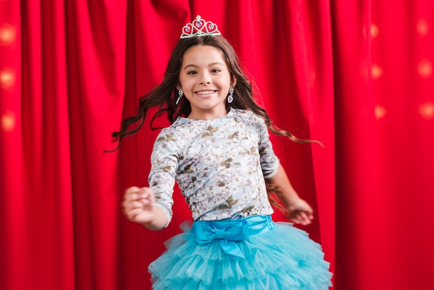 Happy girl in cute dress dancing in front of red curtain