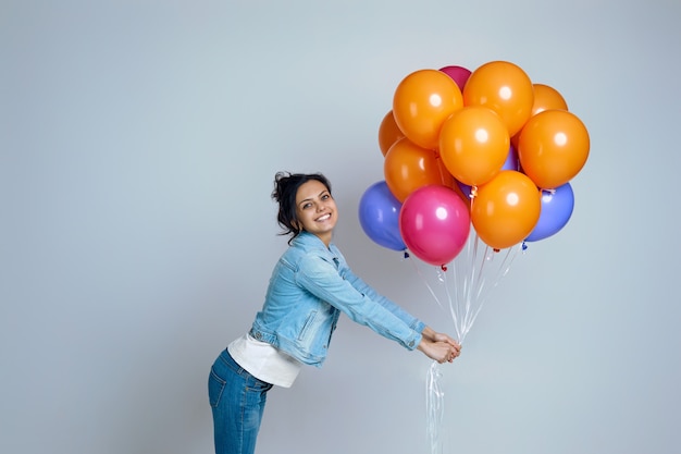 Photo happy girl in denim posing with bright colorful air balloons isolated on gray