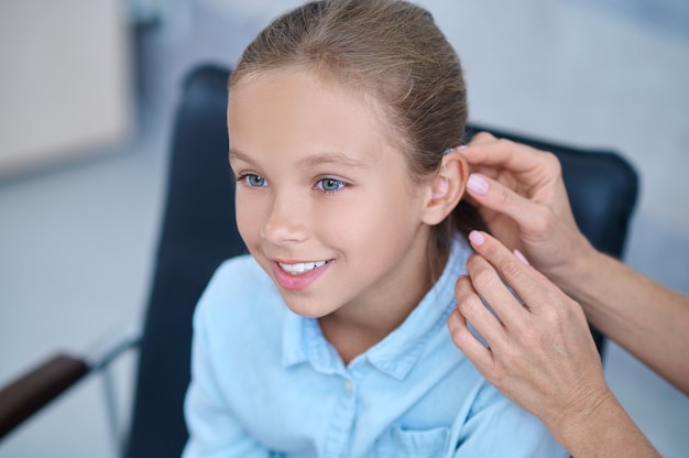 Photo happy girl and doctors hands putting on hearing aid