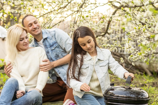 Happy girl, father and mother preparing barbecue in the yard.