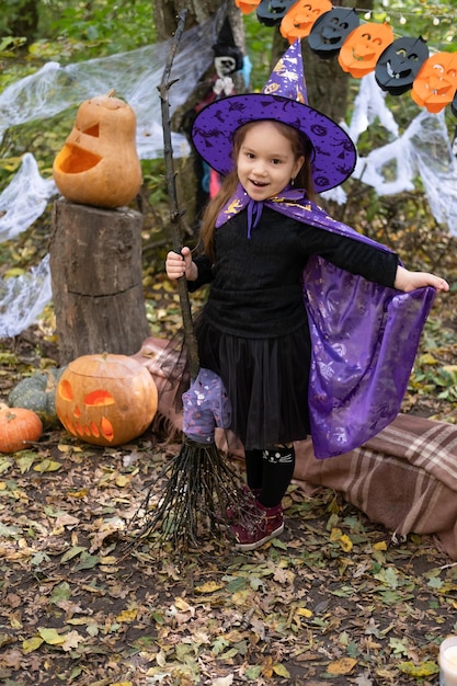 happy girl in halloween costume and witch hat with broom in halloween decoration outdoor