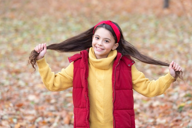 Happy girl holding hair fall outdoors Teenage girl wearing long hair in trendy fall style