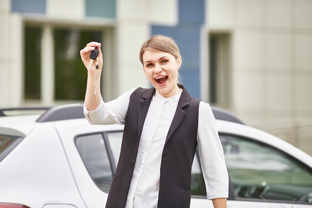 Happy girl holding keys to new car and smiling at camera