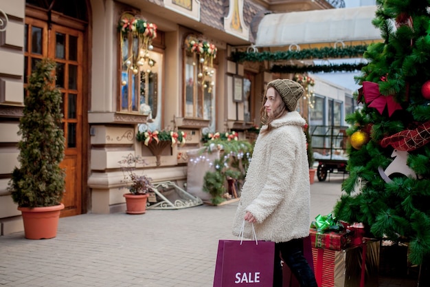 Happy girl holds paperbags with symbol of sale in the stores with sales at Christmas around the city