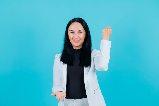 Happy girl is raising up her fists on blue background