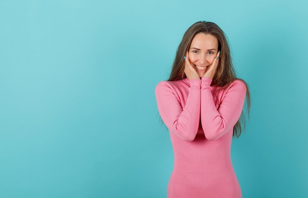 Happy girl is smiling by putting hands on cheeks on blue background