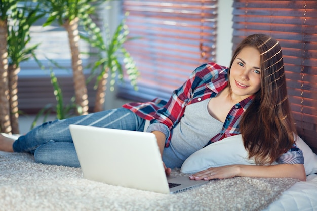 Happy girl lying on the sofa and working on a laptop