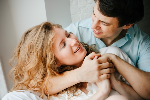 Happy girl and man hugging near window in home. White and blue clothes. Valentine day.