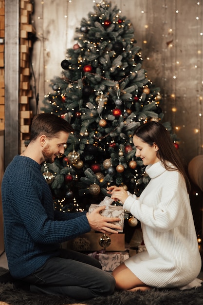 Happy girl opens Christmas gift while sitting near Christmas tree.