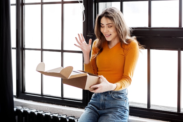 Happy girl opens a corton box at home, delivery, mail and people concept